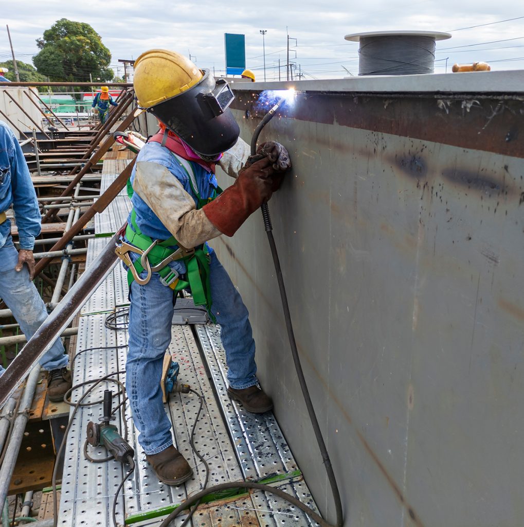 The welder is welding a steel structure work with process Flux C The welder is welding a steel structure work with process Flux Cored Arc Welding(FCAW) and dressed properly with personal protective equipment(PPE) for safety, at industrial factory.