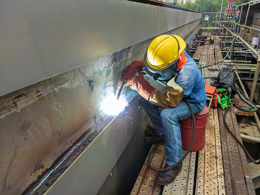 The welder is welding a steel structure work with process Flux C The welder is welding a steel structure work with process Flux Cored Arc Welding(FCAW) and dressed properly with personal protective equipment(PPE) for safety, at industrial factory.
